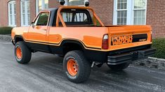 an orange pick up truck parked in front of a brick building