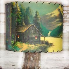 a lamp shade with a painting of a cabin in the woods on it's side