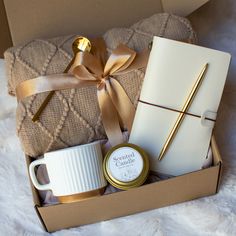 a gift box containing a coffee mug, notebook and pen with a gold bow on it