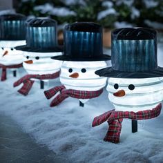 snowmen with hats and scarfs are lined up in the snow, one is wearing a top hat