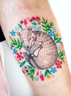 an animal tattoo on the leg of a person with flowers around it and a bear