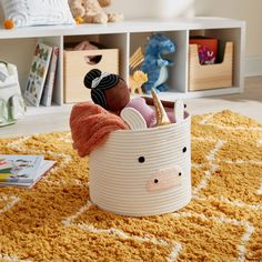 a toy basket with toys in it sitting on a rug next to bookshelves