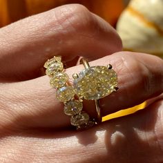 a person's hand holding a ring with yellow and white diamonds on it,