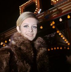 a woman wearing a fur coat standing in front of a carnival ride at night time