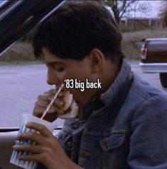 a man sitting in the back seat of a car eating a sandwich and drinking from a cup