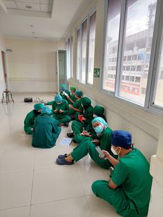 a group of doctors sitting on the floor in green scrubs and masks looking at their phones