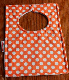 an orange and white polka dot bib on a wooden table with the tag attached to it