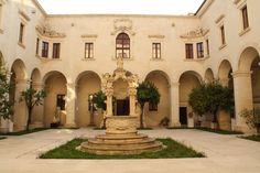 an outdoor courtyard with a fountain in the middle and arches on both sides, surrounded by greenery