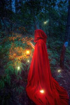 a woman in a red cloak is walking through the woods at night with glowing lights