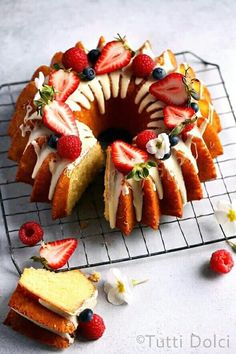 a bundt cake with strawberries and blueberries on top is sitting on a cooling rack