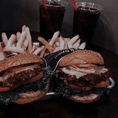 two hamburgers and french fries on a tray with sodas in the back ground