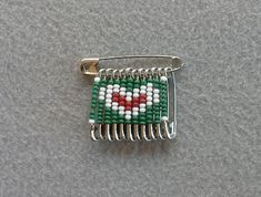 a green and white beaded comb with a heart on it's side, sitting on a gray surface