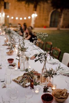 a long table with several vases filled with plants and candles on top of it