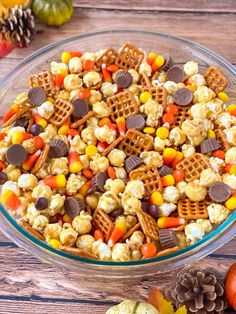 a glass bowl filled with halloween popcorn and candy corn on top of a wooden table