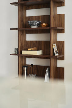 a wooden shelf with books and other items on it in a white walled room that appears to be empty