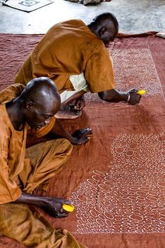 two men sitting on the ground working on an art project with yellow markers in front of them