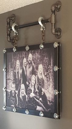 an old photo hangs on the wall above a pipe - fitting faucet, which has been decorated with metal pipes and rivets