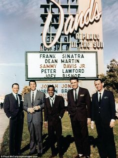 a group of men standing next to each other in front of a sign that says sands