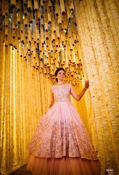 a woman in a pink dress standing next to a yellow curtain with beads hanging from it