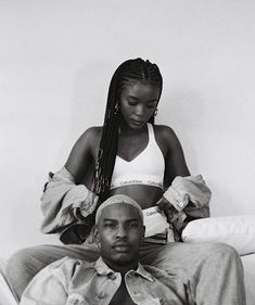 a man sitting next to a woman on top of a bed in front of a white wall