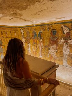 a woman sitting at a table in front of an egyptian wall painting on the side of a building