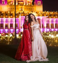 two women standing next to each other in front of a building with lights on it