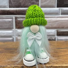 a green and white knitted doll sitting on top of a wooden table