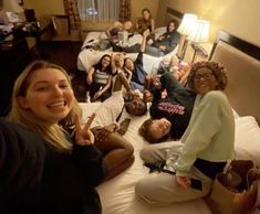 a group of people laying on top of a bed in a hotel room with one woman giving the peace sign