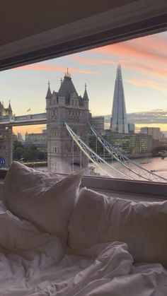 a bed with white sheets and pillows in front of a window overlooking the london skyline