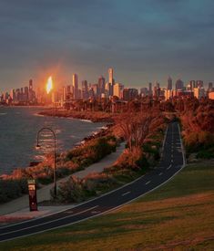 the sun is setting over a large city by the water and trees in front of it