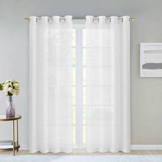 a white curtain hanging on the side of a wall next to a vase with flowers