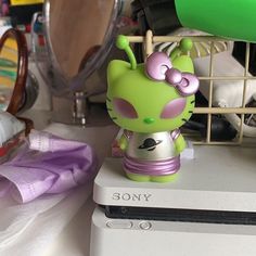 a small green toy sitting on top of a white laptop computer next to a hair dryer