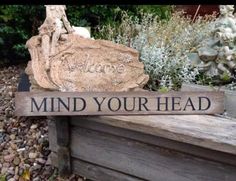 a wooden sign that says,'welcome to the garden mind your head'on it