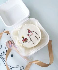 a decorated cookie in a plastic container with a brown ribbon around it and an image of a unicorn on the front