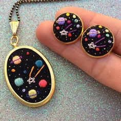 a hand holding two pendants with space and stars on them, next to a chain