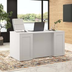 an office desk with a laptop on it in front of a large window overlooking the water