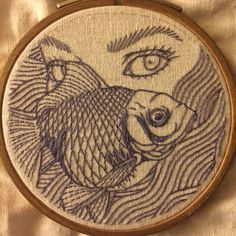 a close up of a embroidery on a piece of cloth with an eye in the background