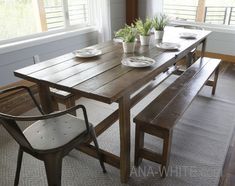 a wooden table with two chairs and plates on it in front of a large window