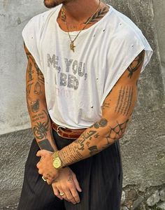 a man with tattoos on his arm and chest standing in front of a stone wall