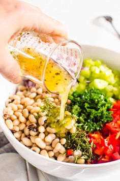 someone pouring dressing into a bowl filled with beans, broccoli and other vegetables