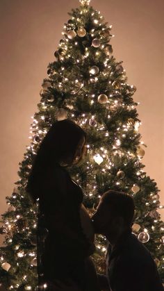 a man and woman standing in front of a christmas tree with lights on the branches