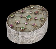 an ornate silver box with colorful stones on it's sides and a black background