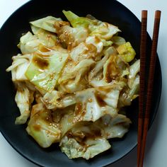 a black plate topped with cabbage covered in sauce and chopsticks next to it