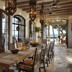 a dining room table surrounded by chairs and hanging lights in front of an open patio