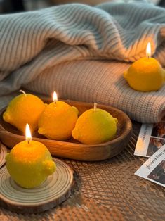 three lemons in a wooden bowl on a table with two tea lights and pictures