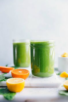 two jars filled with green smoothie next to sliced oranges