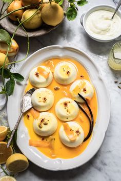 a white plate topped with dumplings covered in sauce next to lemons and other fruit