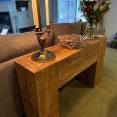 a wooden table with two candles on it in front of a couch and vase filled with flowers