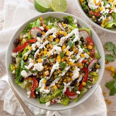 two white bowls filled with salad on top of a table next to lime wedges