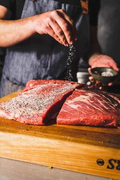 a man is sprinkling seasonings on raw meat while standing in front of a cutting board